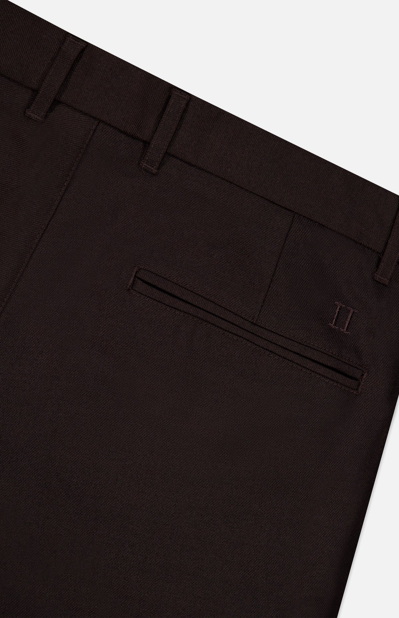 Close-up of the back pocket area of the LES DEUX Brushed Twill Regular Suit Pants in dark brown, crafted from brushed twill fabric, featuring a single welt pocket, belt loops, and a subtle embroidered II logo near the pocket.