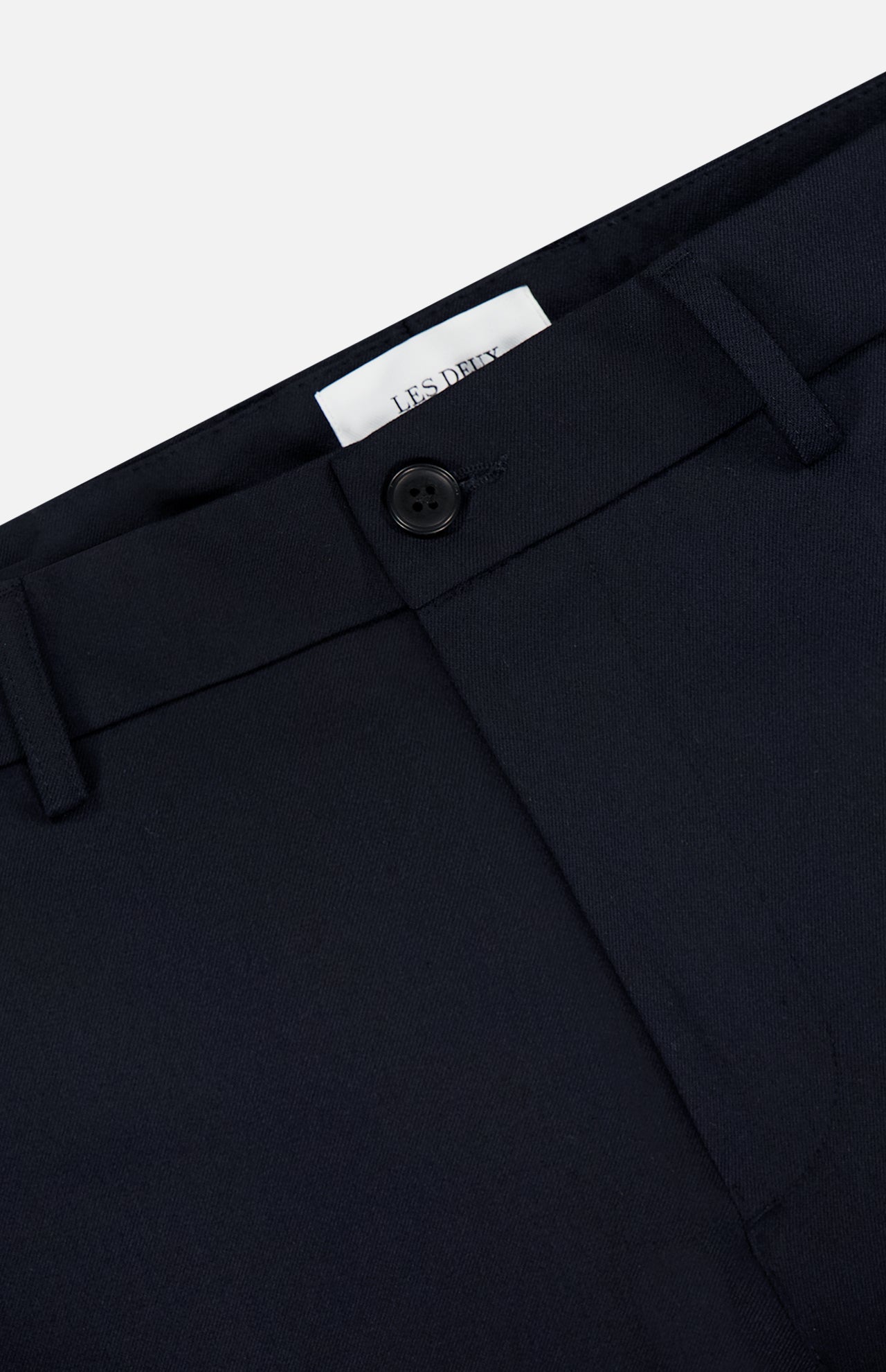 Close-up of the waistband and upper section of LES DEUX Como Reg Suit Pants in black, showing a single button closure, belt loops, and a partially visible white label inside.