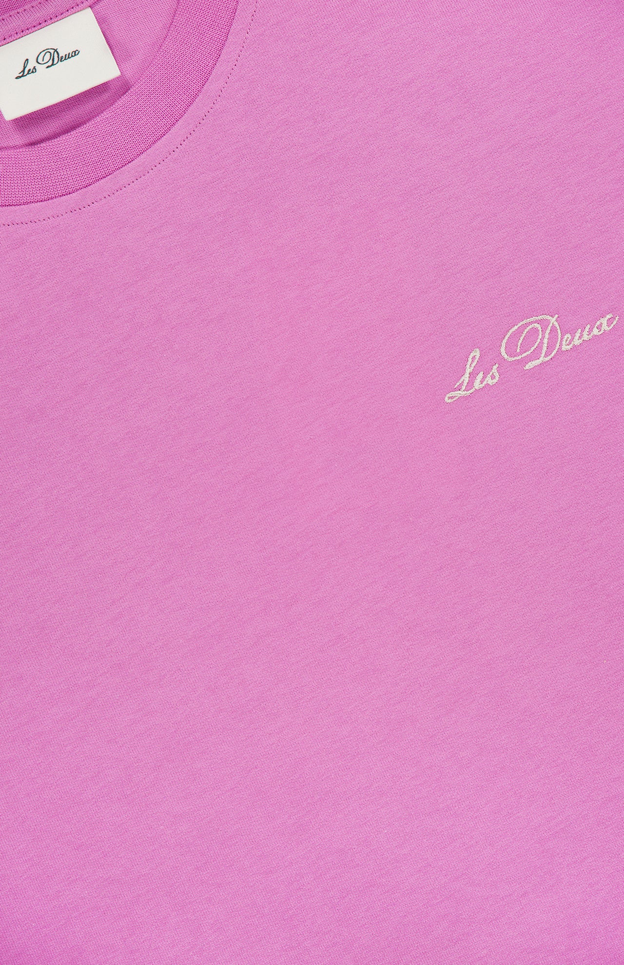 A close-up of the Crew Neck Logo T-shirt by LES DEUX in bright pink, featuring the brand's name stitched in white on the chest and a visible LES DEUX label inside the neckline—ideal for standout casual wear.