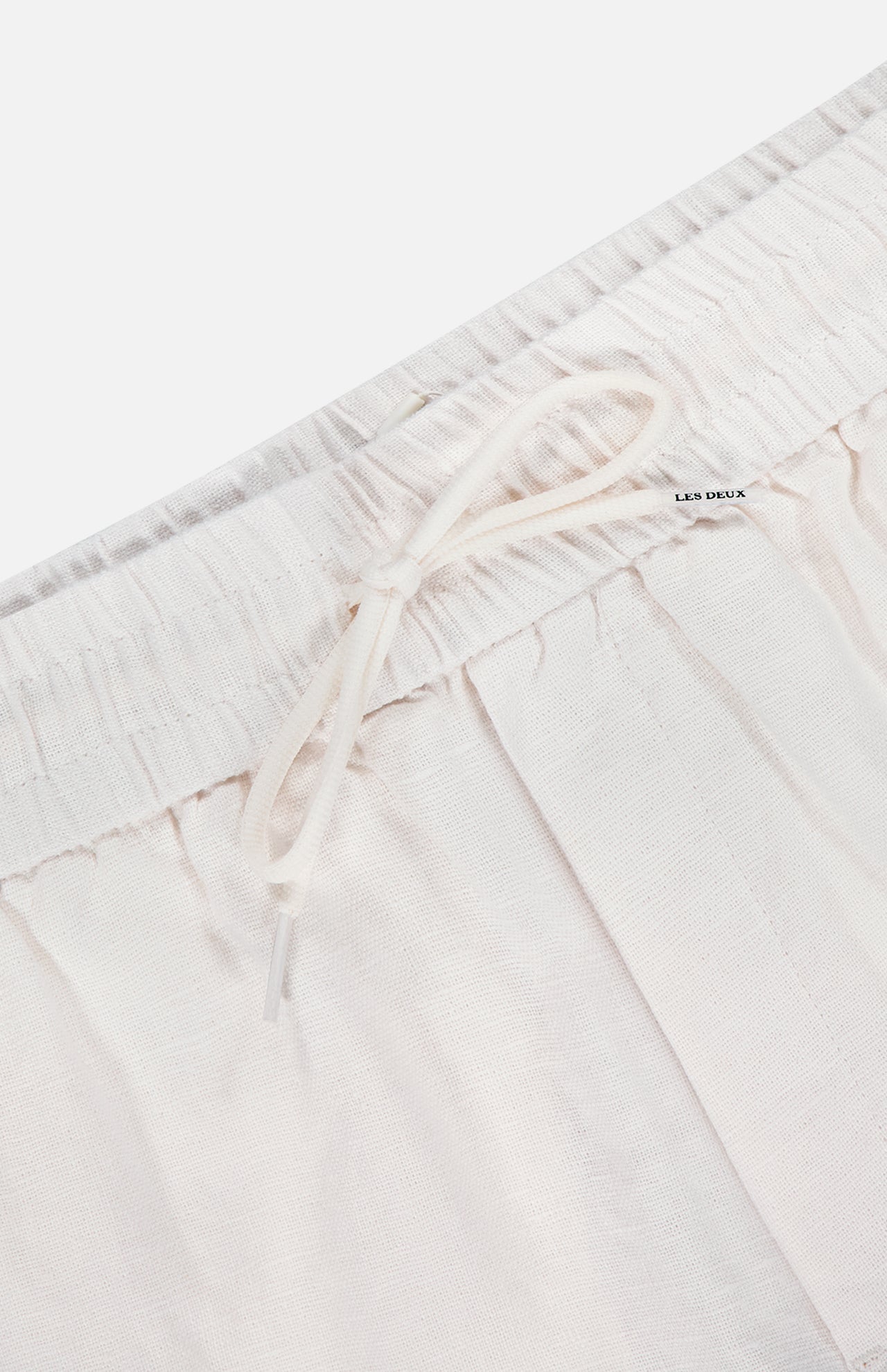 Close-up of the waistband on LES DEUX Patrick Linen-blend Pants, showing breathable light beige fabric, an elastic band with drawstring waist, and a small LES DEUX tag near the top.