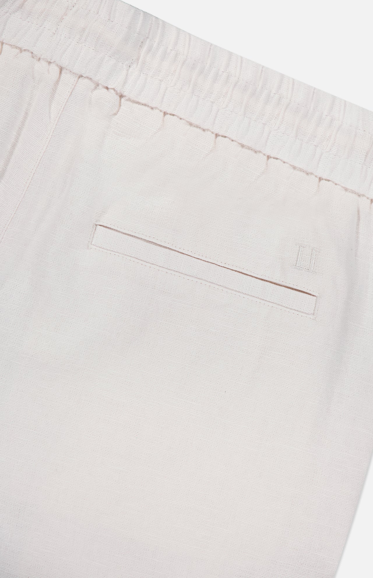 Close-up of the back of LES DEUX Patrick Linen-blend Pants, showcasing breathable light beige fabric, an elastic waistband, and a single welt pocket.