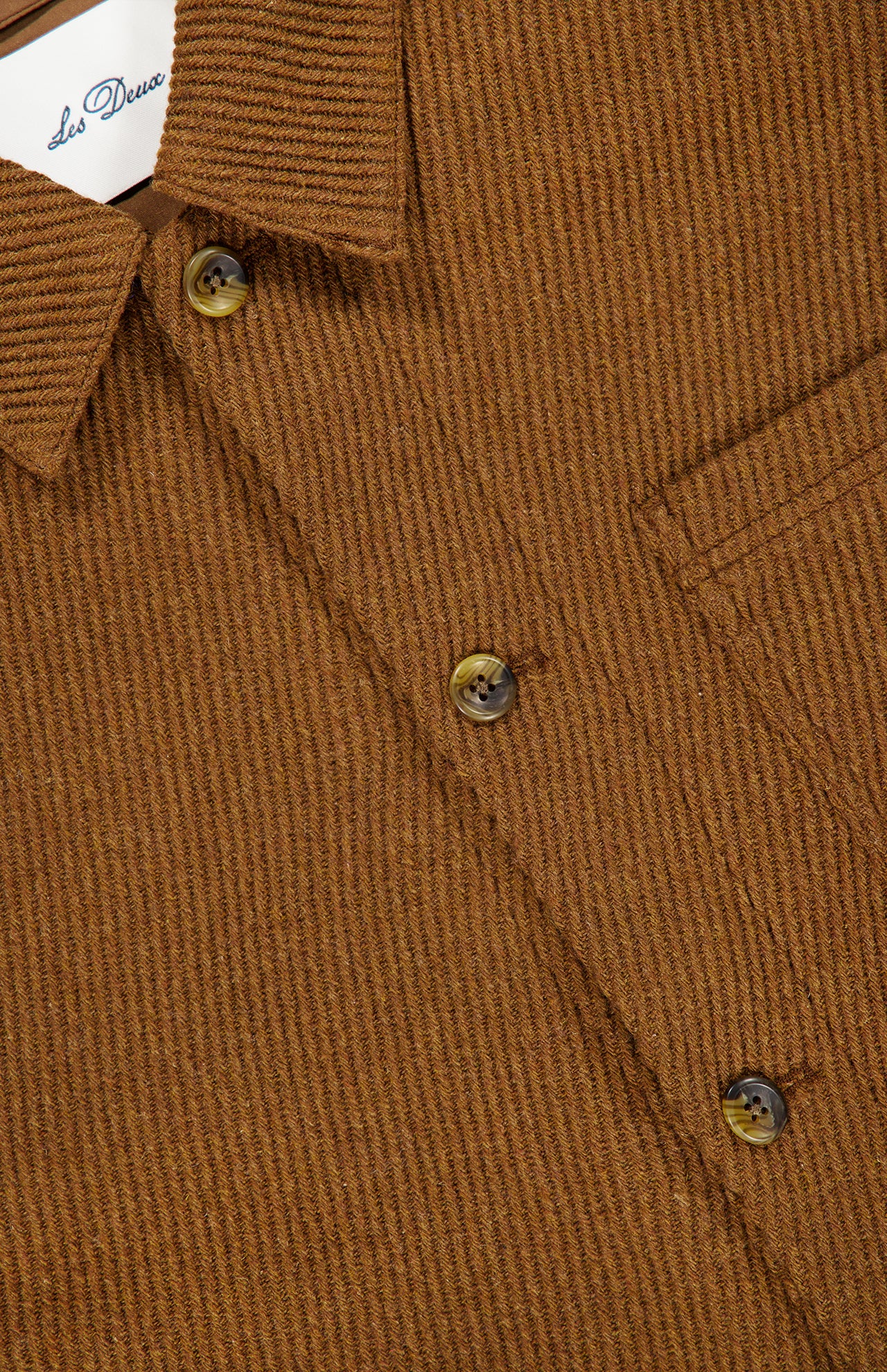 Close-up of the LES DEUX Twill Wool Overshirt for men, featuring a brown ribbed texture, classic collar, three-button placket, and a glimpse of the chest pocket. A partially visible label appears inside the collar.