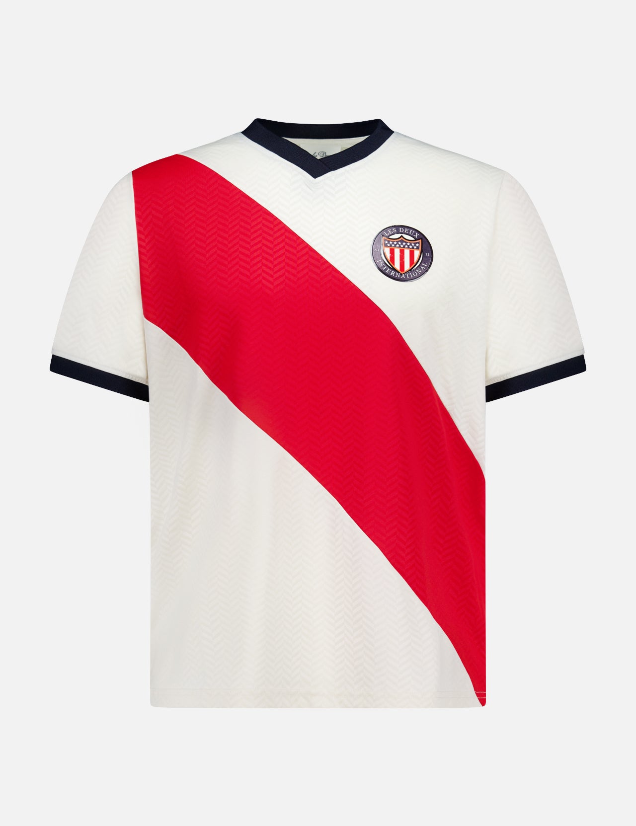 The LES DEUX USA Football Jersey is a white short-sleeve shirt with a bold red diagonal stripe, blue V-neck collar and sleeve trim, plus a club crest with red and white stripes on the left chest.