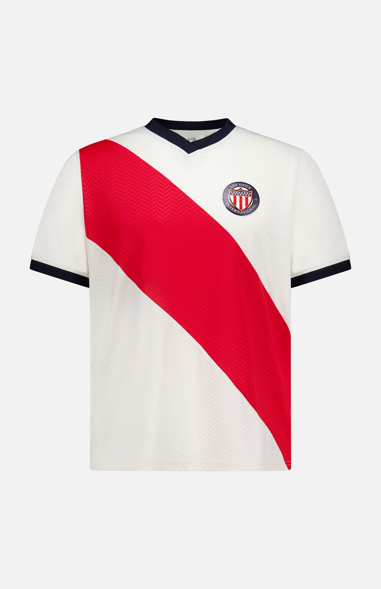 The LES DEUX USA Football Jersey is a white short-sleeve shirt with a bold red diagonal stripe, blue V-neck collar and sleeve trim, plus a club crest with red and white stripes on the left chest.