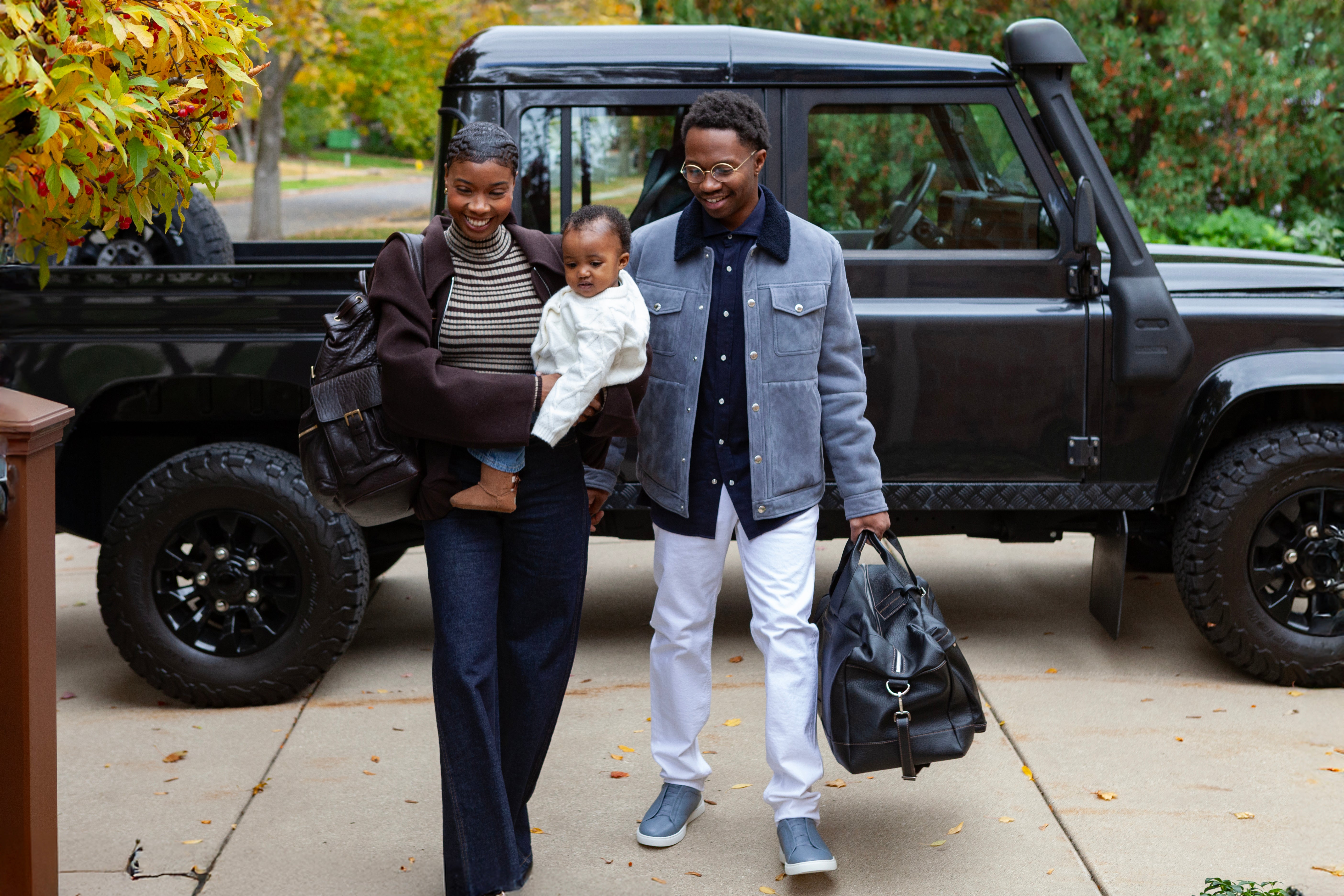Family of three walking outdoors with a black SUV in the background