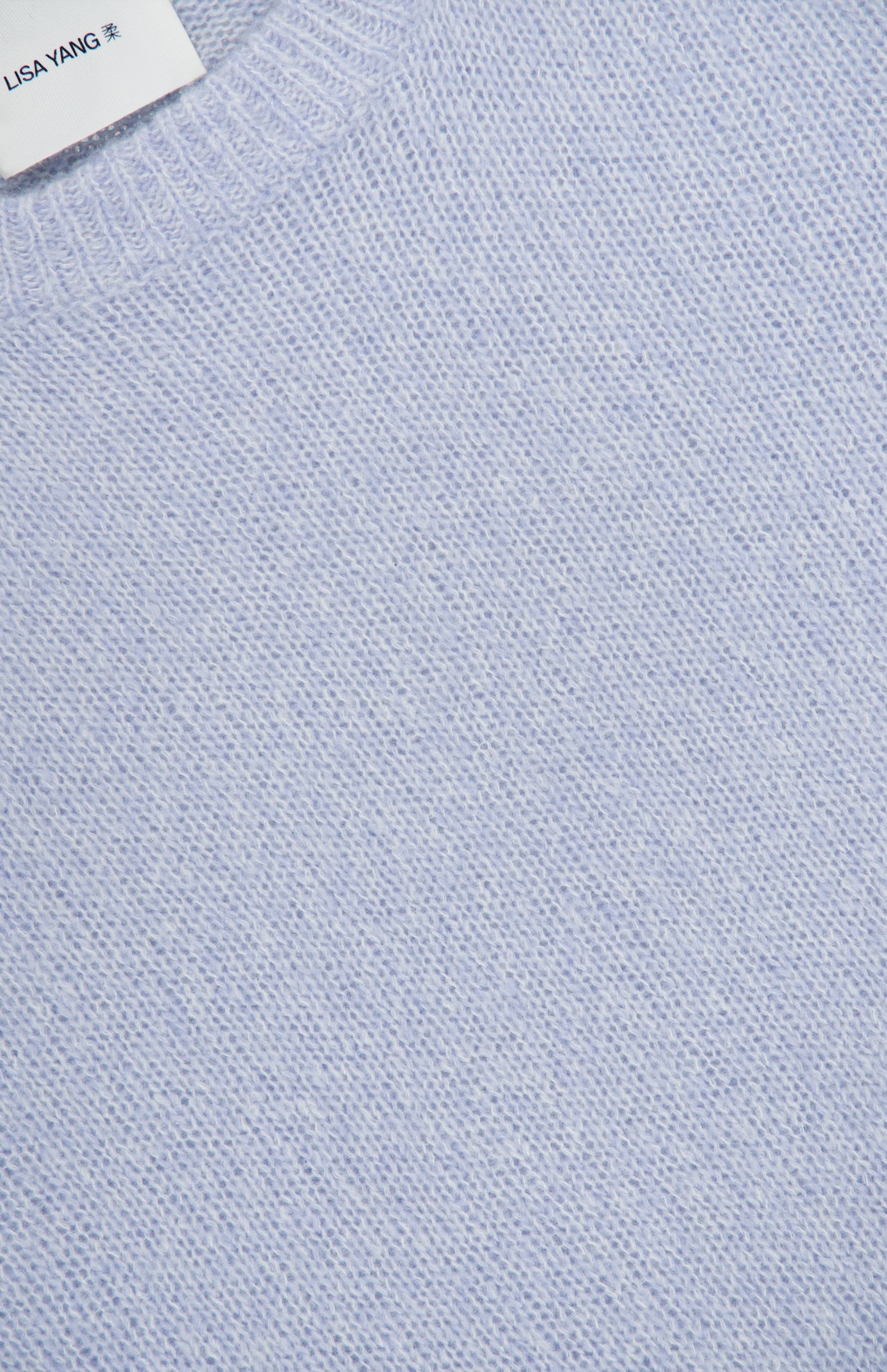 Close-up of the LISA YANG Lova Cashmere and Silk Sweater, featuring a soft, light blue knit with a ribbed collar that reflects a refined Scandinavian aesthetic. A white tag bearing the LISA YANG brand is partially visible at the top left corner.
