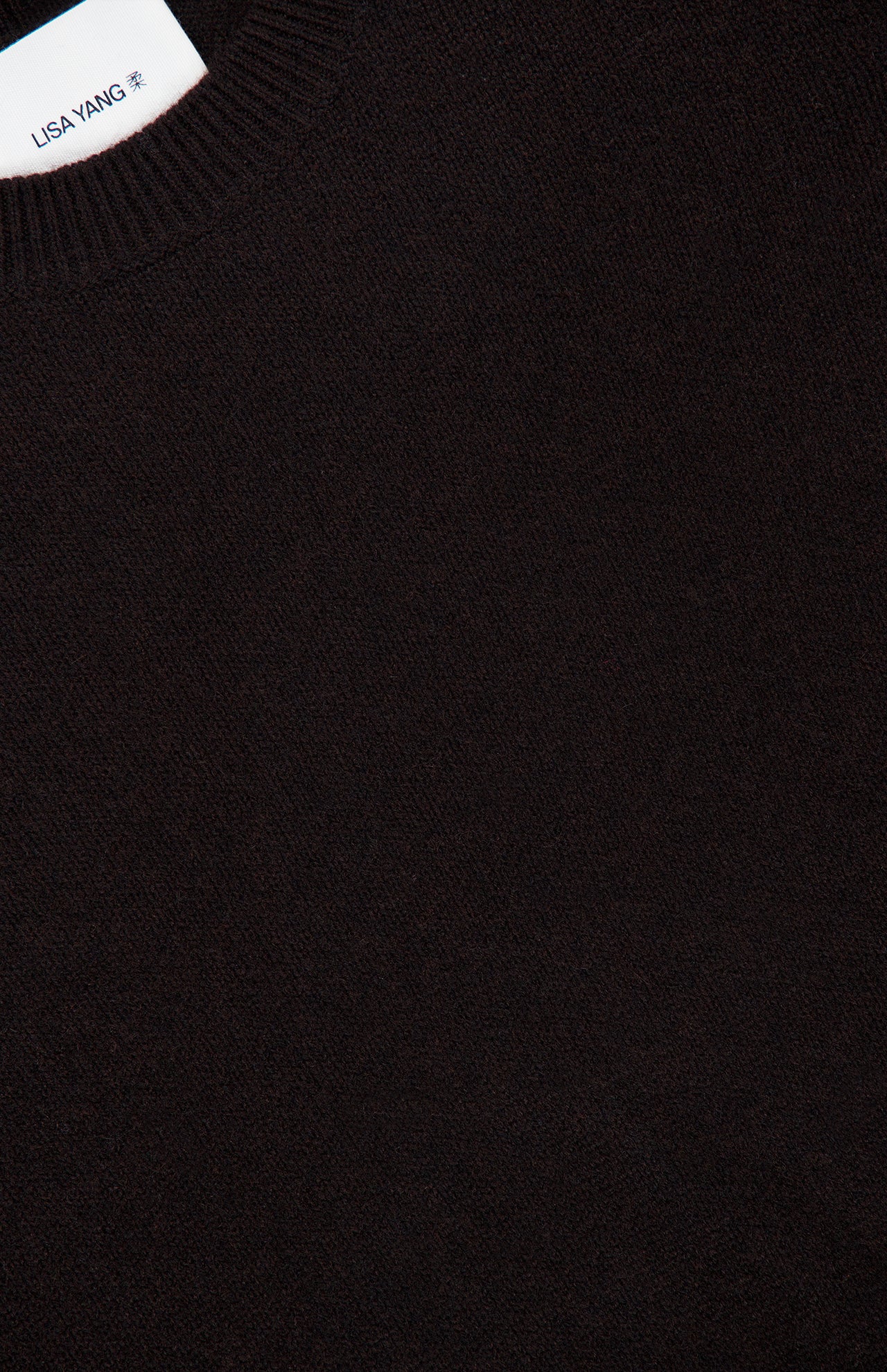Close-up of the Mable Cashmere Sweater in dark brown, featuring a ribbed crew neckline and a white LISA YANG label sewn inside the collar, exemplifying a refined Scandinavian aesthetic.