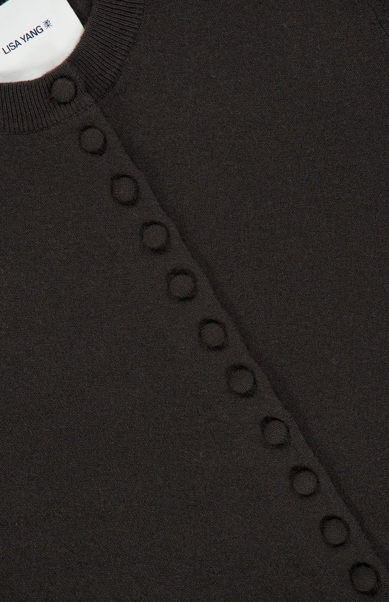 Close-up of the Wilona Cardigan Sweater, a luxury cashmere dark brown piece by LISA YANG, featuring a row of circular knit details along the front and a visible white label with the brand name.
