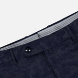 Close-up of the waistband of Malcom’s Wool Cashmere Camo Trouser Pant in dark blue patterned fabric, featuring a black button, belt loops, and a partially visible gray striped inner lining. Expertly crafted in Italy from luxurious wool cashmere.