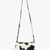 The MANSUR GAVRIEL Mini Gaia Cow Print Crossbody Bag features a black and white cow pattern, a small rectangular shape, and a long adjustable strap, showcased against a plain white background.