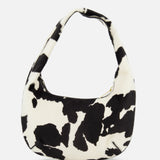 The MANSUR GAVRIEL Mini Gnocchi Cow Print Bag features a black-and-white cow pattern and a curved handle, shown against a plain white background.