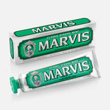 A tube of MARVIS Classic Strong Mint Toothpaste, in green and white, is displayed alongside its coordinating box—both adorned with the MARVIS logo and signature decorative details. This Italian-made toothpaste offers a concentrated formula that provides the bold, classic strong mint flavor for a refreshing clean.