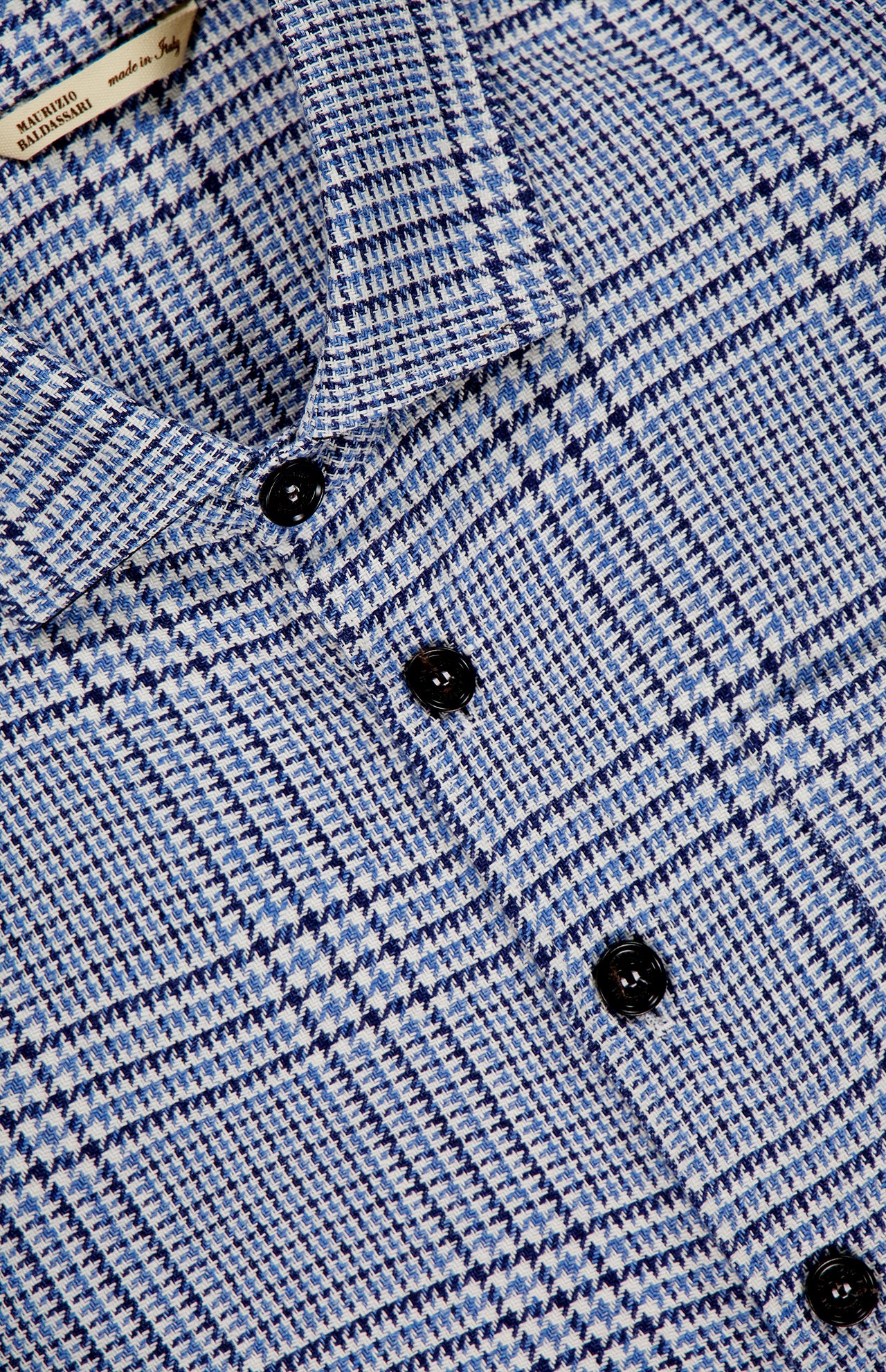 Close-up of the MAURIZIO BALDASSARI Classic Pockets Plaid Overshirt in blue and white, showcasing a micro houndstooth checkered pattern, black buttons, and a “Made in Italy” tag. Expertly crafted from a premium hemp wool blend, this elevated overshirt combines refined texture with classic style.