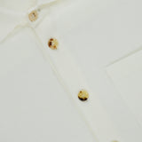 Close-up of the Solferino Wool Overshirt by MAURIZIO BALDASSARI, an off-white Italian-made piece featuring a white collar, chest pocket, and four beige buttons—one fastened at the top and three left unfastened below.
