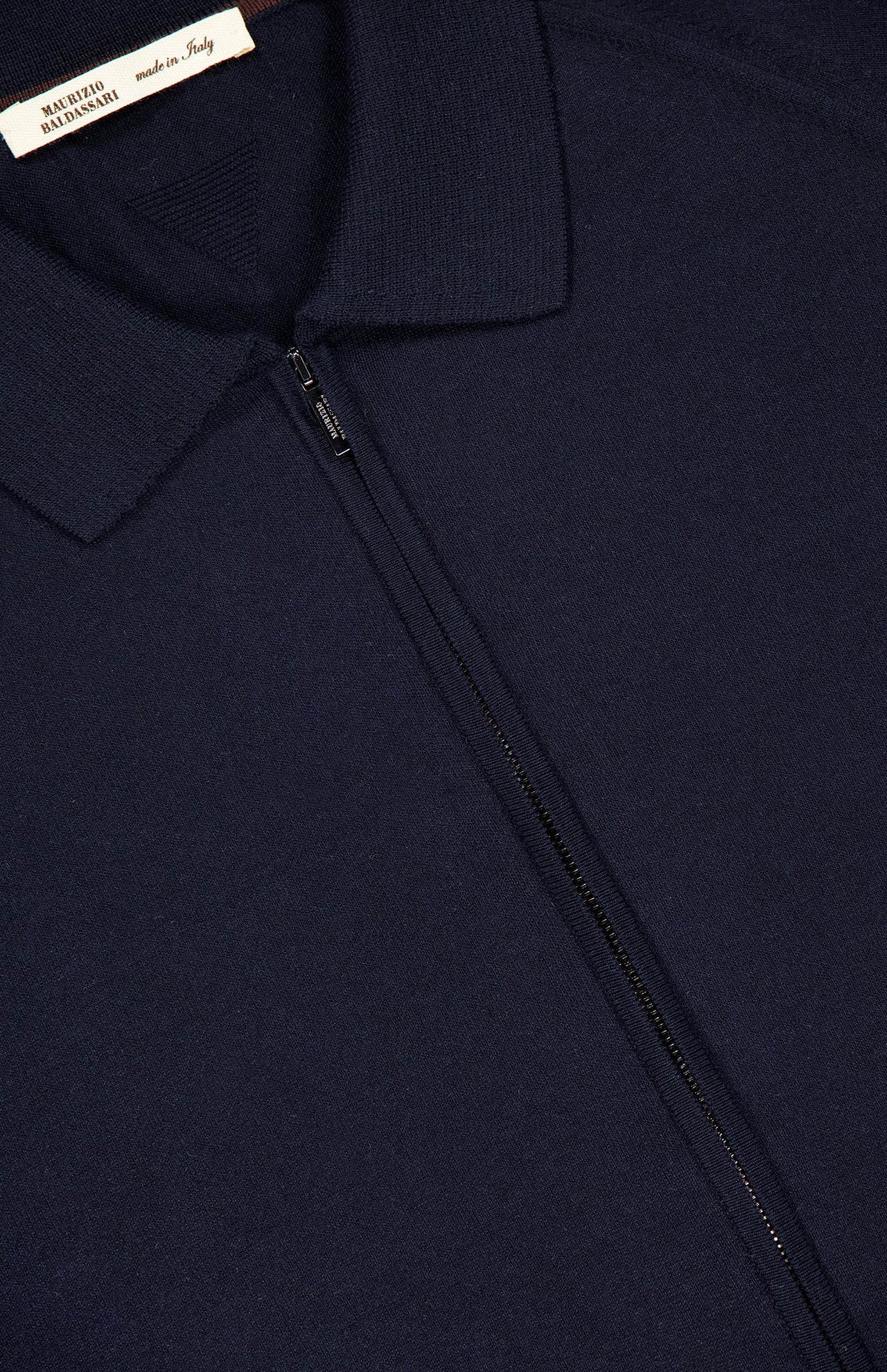 Close-up of the MAURIZIO BALDASSARI Tennis Details Zip Sweater in navy, featuring a center zip-up collar and a visible "made in Italy" label at the neckline. The fabric appears soft and finely knit.