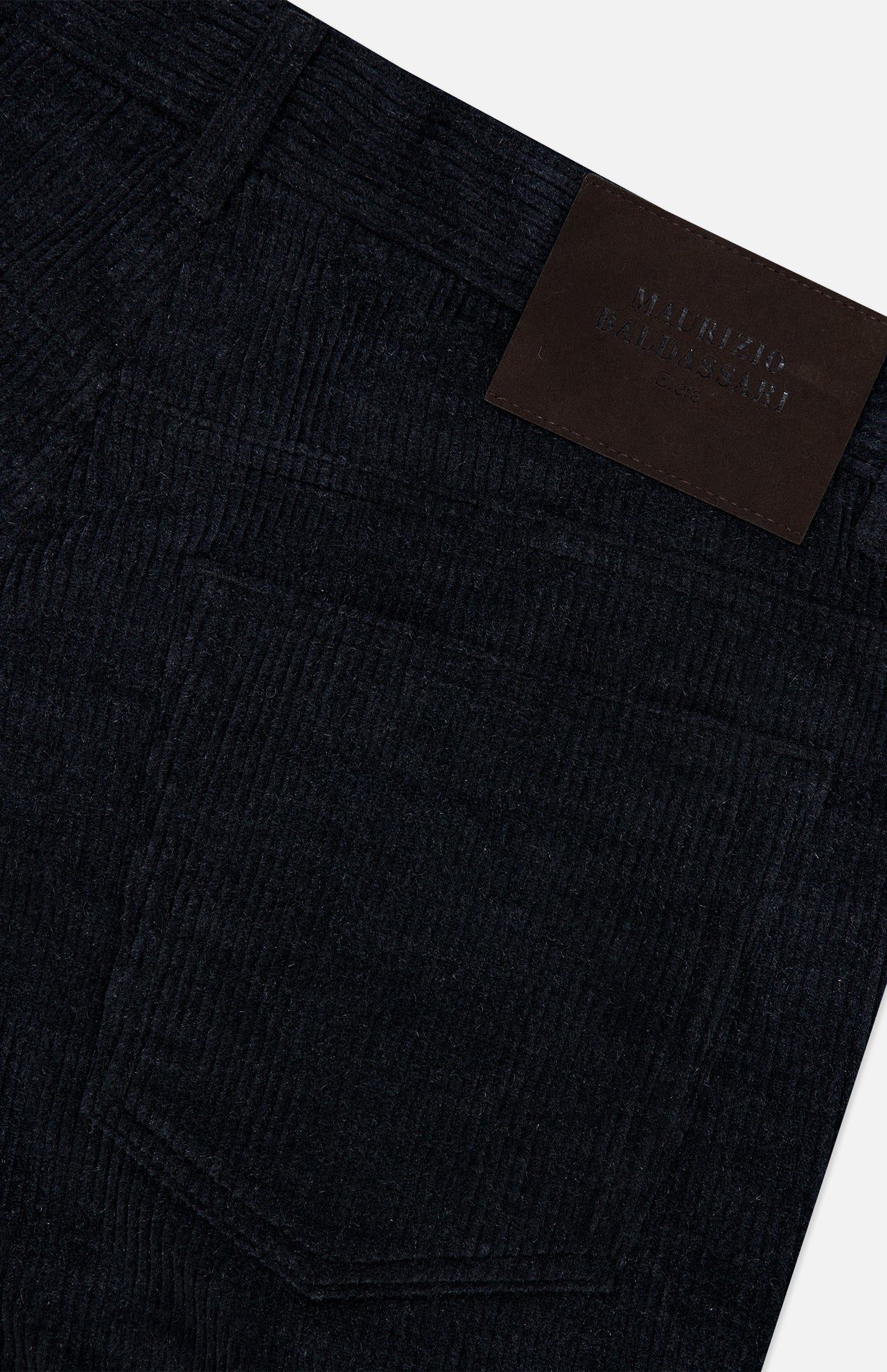 Close-up of the MAURIZIO BALDASSARI Treves Five Pocket Corduroy Pants in black, featuring a detailed view of the back pocket and a black leather patch with embossed, partially readable text on the waistband. The visible fabric texture and precise stitching showcase the refined Italian craftsmanship.