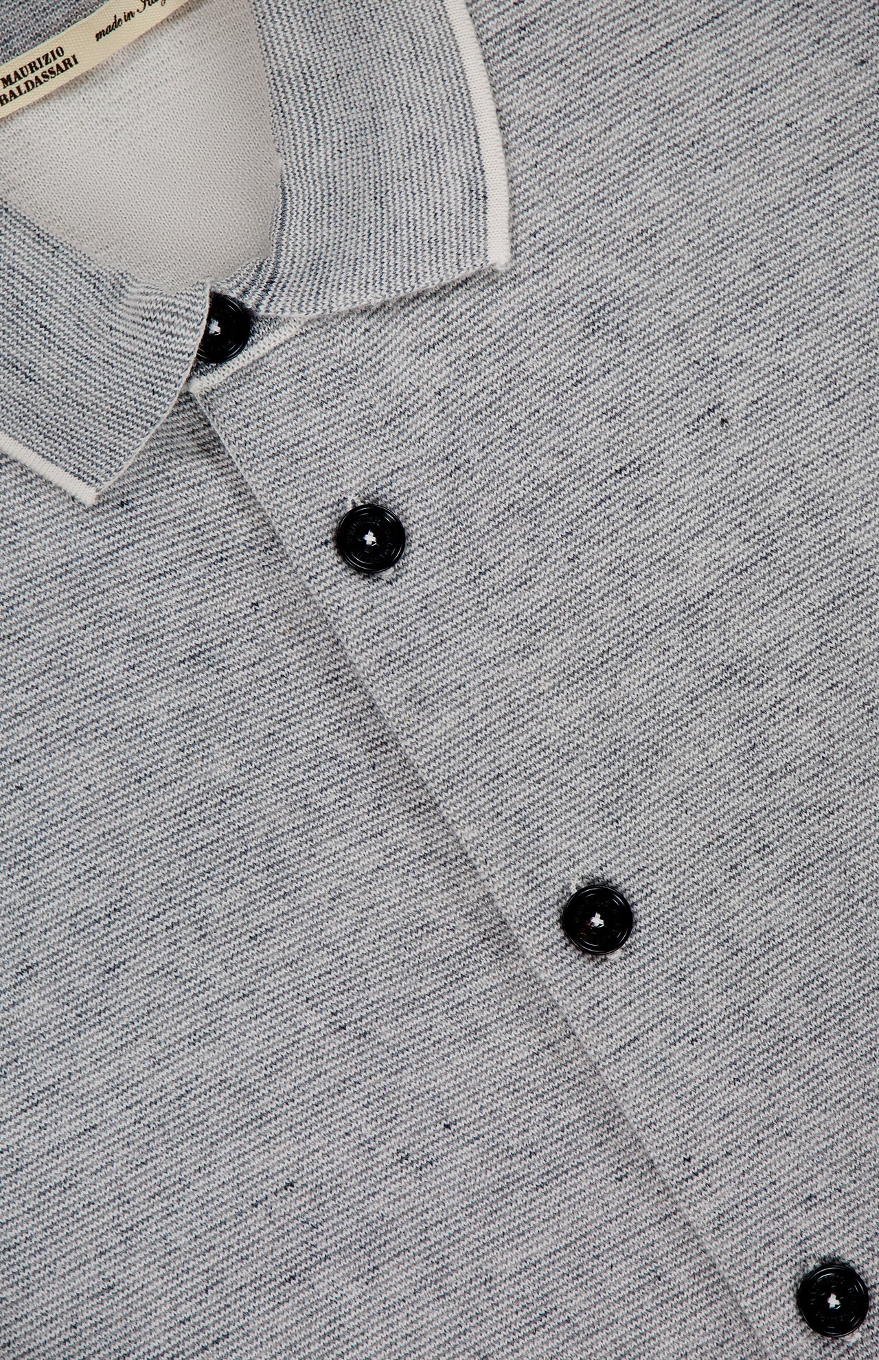 Close-up of the MAURIZIO BALDASSARI Millerighe Milano Stitch Overshirt in light grey virgin wool linen, featuring a white-trimmed collar, black buttons, textured weave, and a visible "made in Italy" shirt label inside the collar.