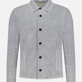 The Millerighe Milano Stitch Overshirt by MAURIZIO BALDASSARI is a light grey, long-sleeved collared jacket with black buttons and two front pockets with white trim, crafted from virgin wool linen in Italy and shown on a plain white background.