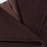 Close-up of a dark brown MAX MARA Wrap Trench Coat lapel featuring a branded label at the collar and a small white cross stitch detail on the lower edge.
