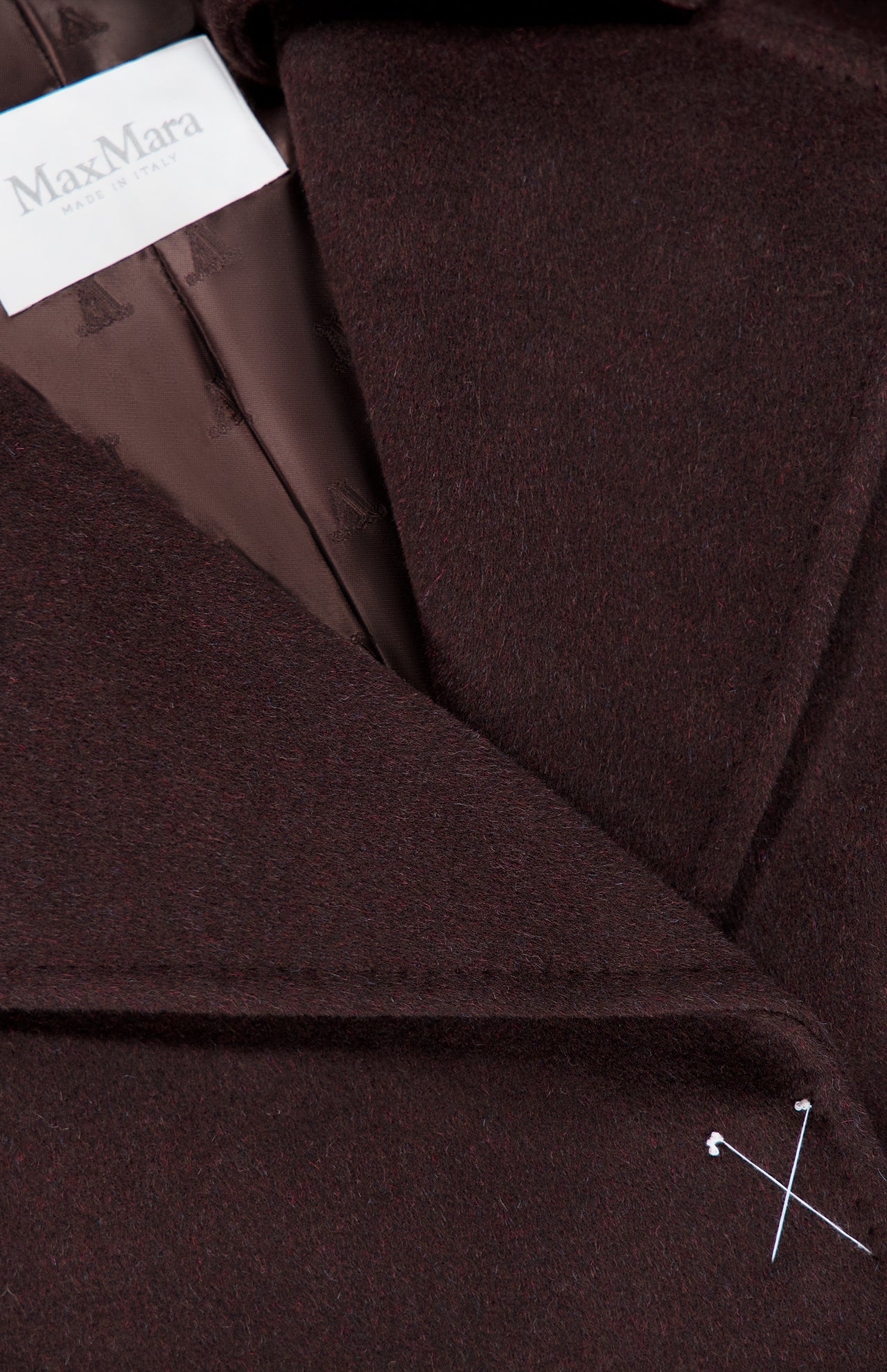 Close-up of a dark brown MAX MARA Wrap Trench Coat lapel featuring a branded label at the collar and a small white cross stitch detail on the lower edge.