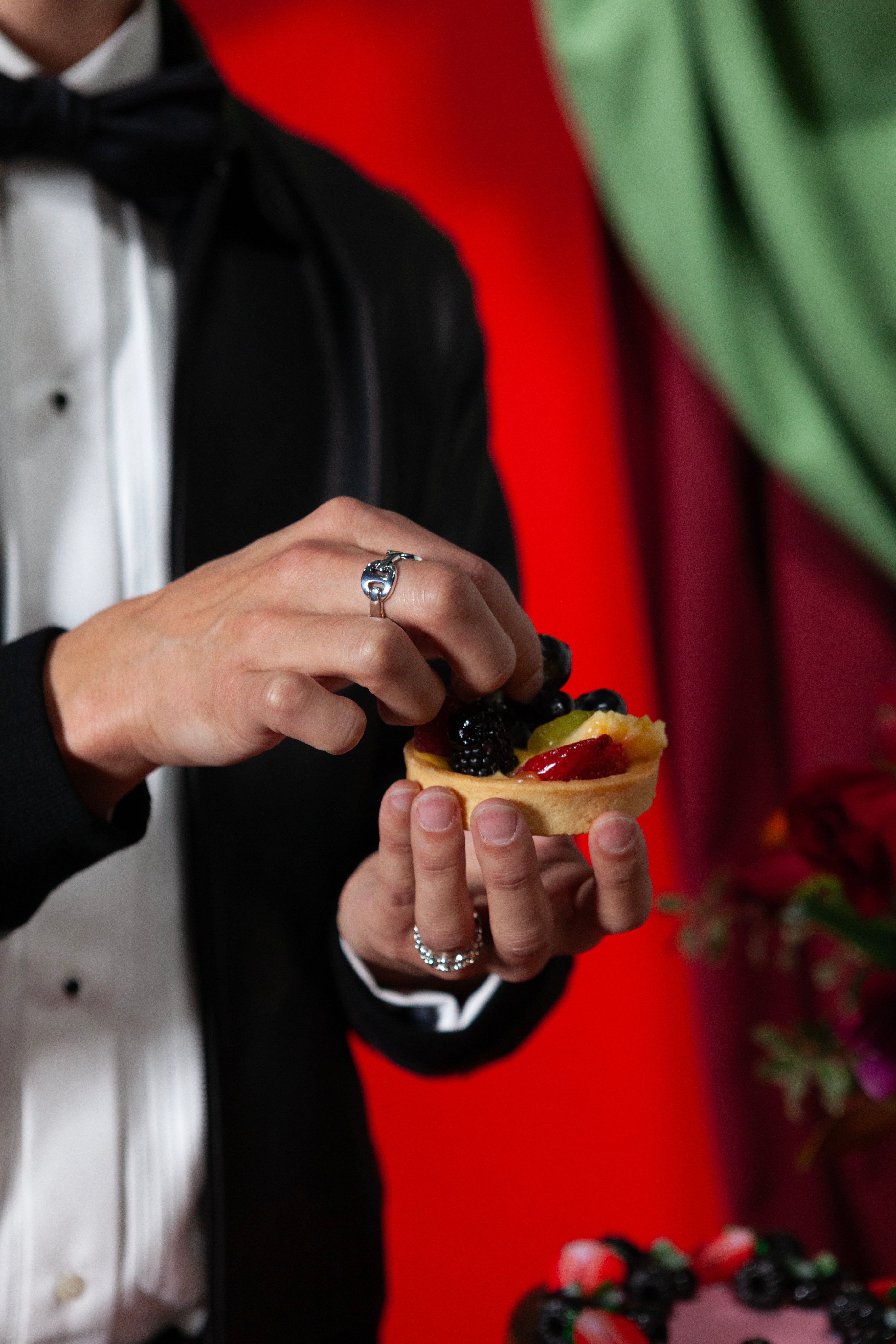 Person in formal attire holding a small appetizer with berries against a red and green background