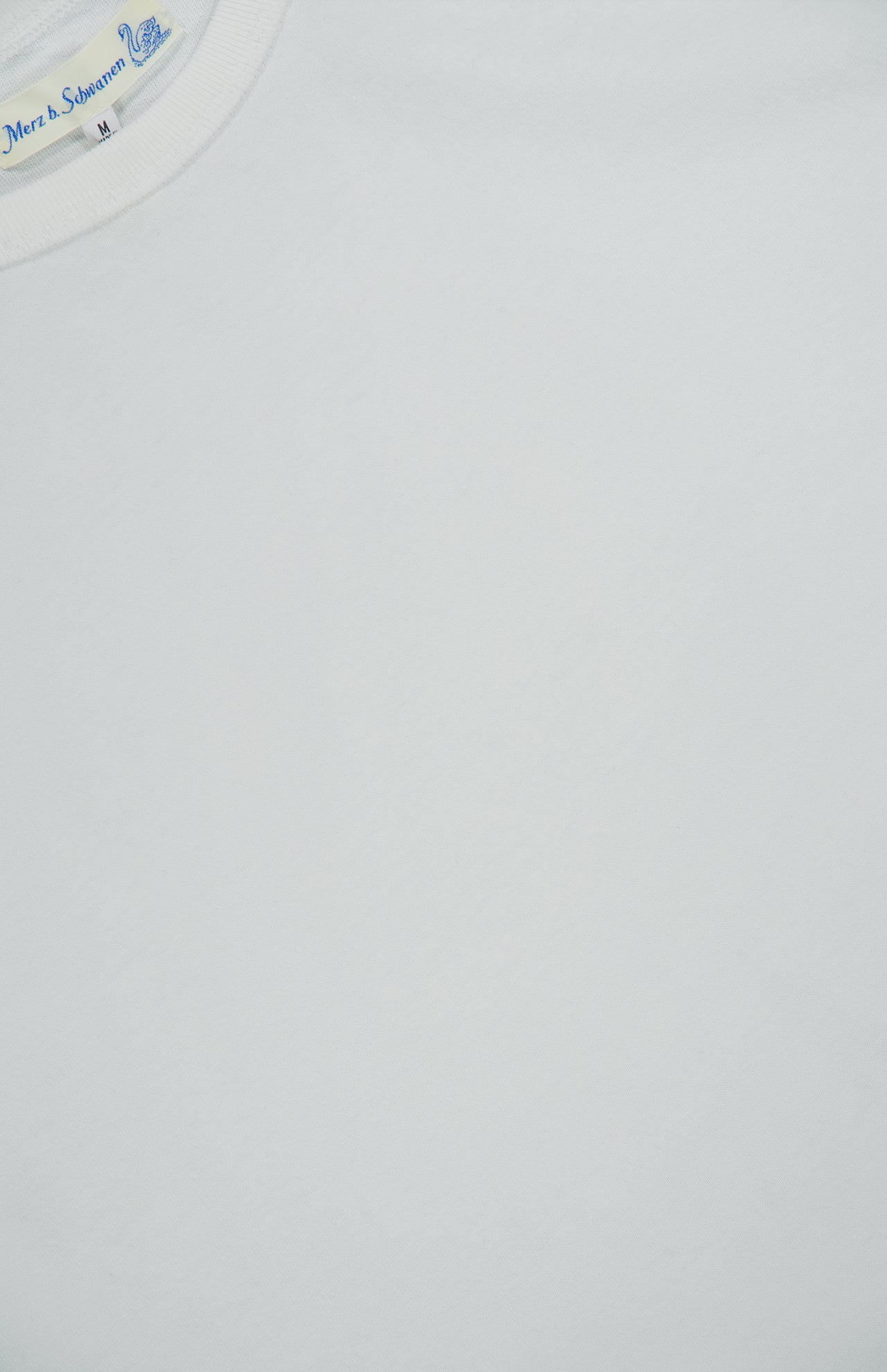 Close-up of the Merz B. Schwanen Classic Jersey T-shirt, crafted from mid-weight jersey fabric. A small clothing tag with blue text is visible near the neckline. The shirt appears clean and smooth with minimal wrinkles, highlighting heritage craftsmanship in its simple yet refined details.