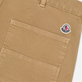 Close-up of MONCLER Stretch Cotton Cargo Trouser Pants in tan, featuring a large front pocket, small round logo patch above the pocket near a belt loop, and sturdy textured fabric for a utility-inspired design.