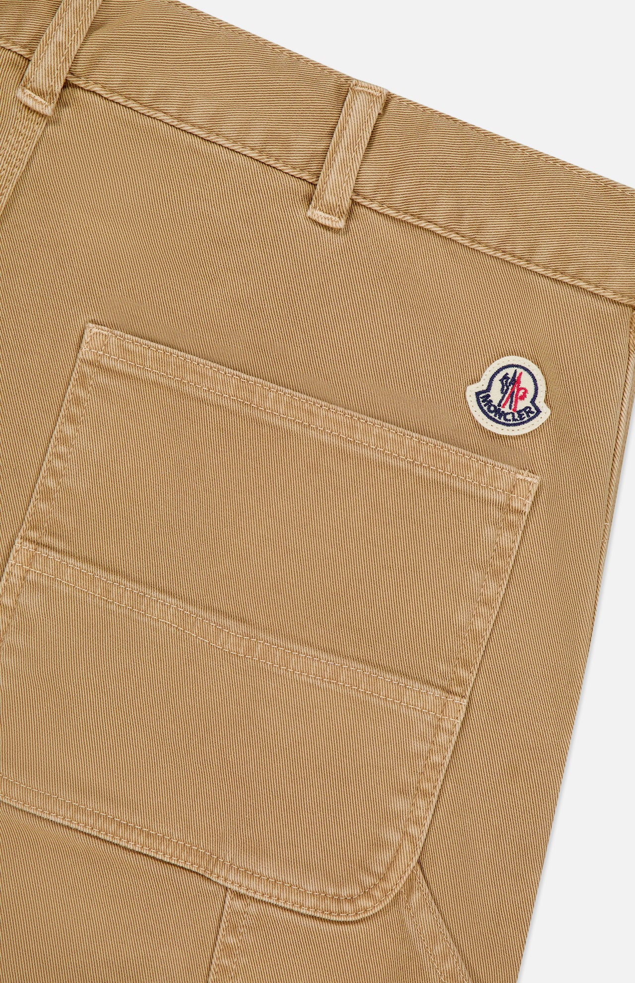 Close-up of MONCLER Stretch Cotton Cargo Trouser Pants in tan, featuring a large front pocket, small round logo patch above the pocket near a belt loop, and sturdy textured fabric for a utility-inspired design.