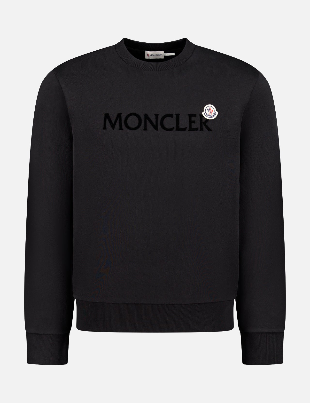 The MONCLER Crewneck Long Sleeve Sweatshirt features bold chest lettering and a small round logo patch above. Made from black cotton jersey, it’s ideal ski travel outerwear with long sleeves and a classic crewneck design.