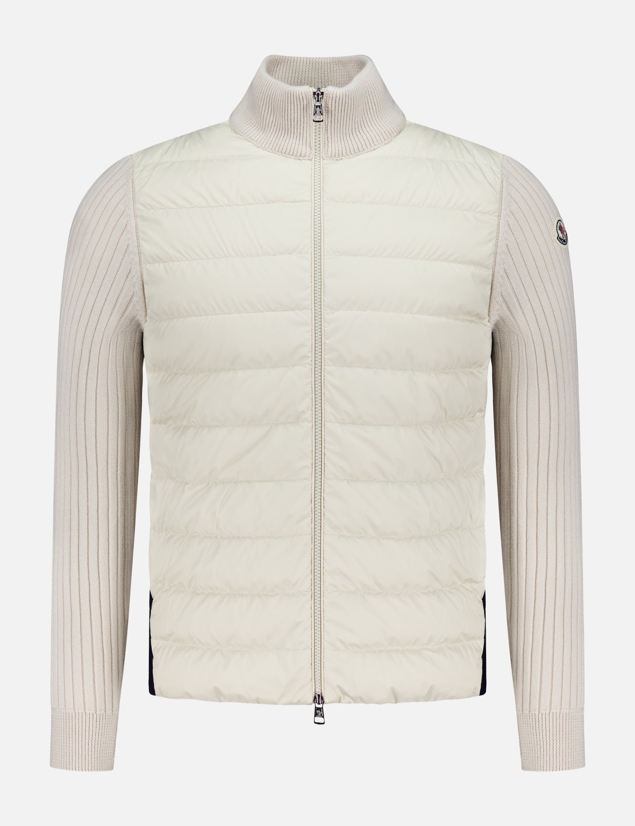 The MONCLER Hybrid Zip Up Jacket features a cream color, ribbed knit sleeves and collar, horizontal quilted front stitching, and a small logo patch on the upper left sleeve—ideal cold-weather outerwear.