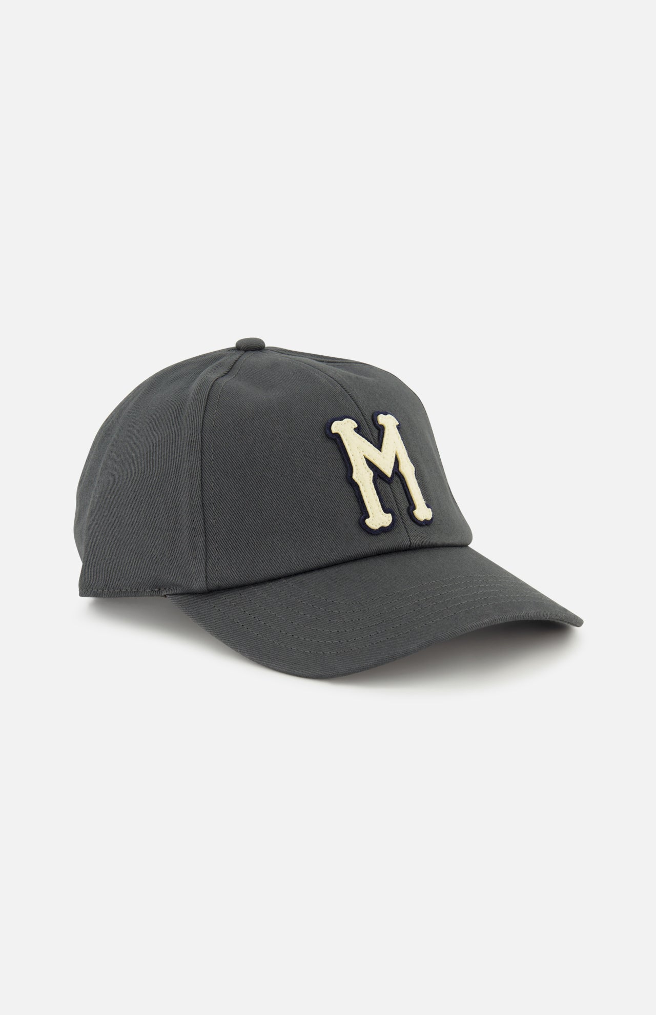 The Monogram Baseball Cap by MONCLER is a dark grey cap with a curved brim, featuring a large white "M" embroidered on the front.