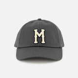 The MONCLER Monogram Baseball Cap features a grey design with a cream-colored embroidered letter M on the front, inspired by designer outerwear style, and is shown against a plain white background.