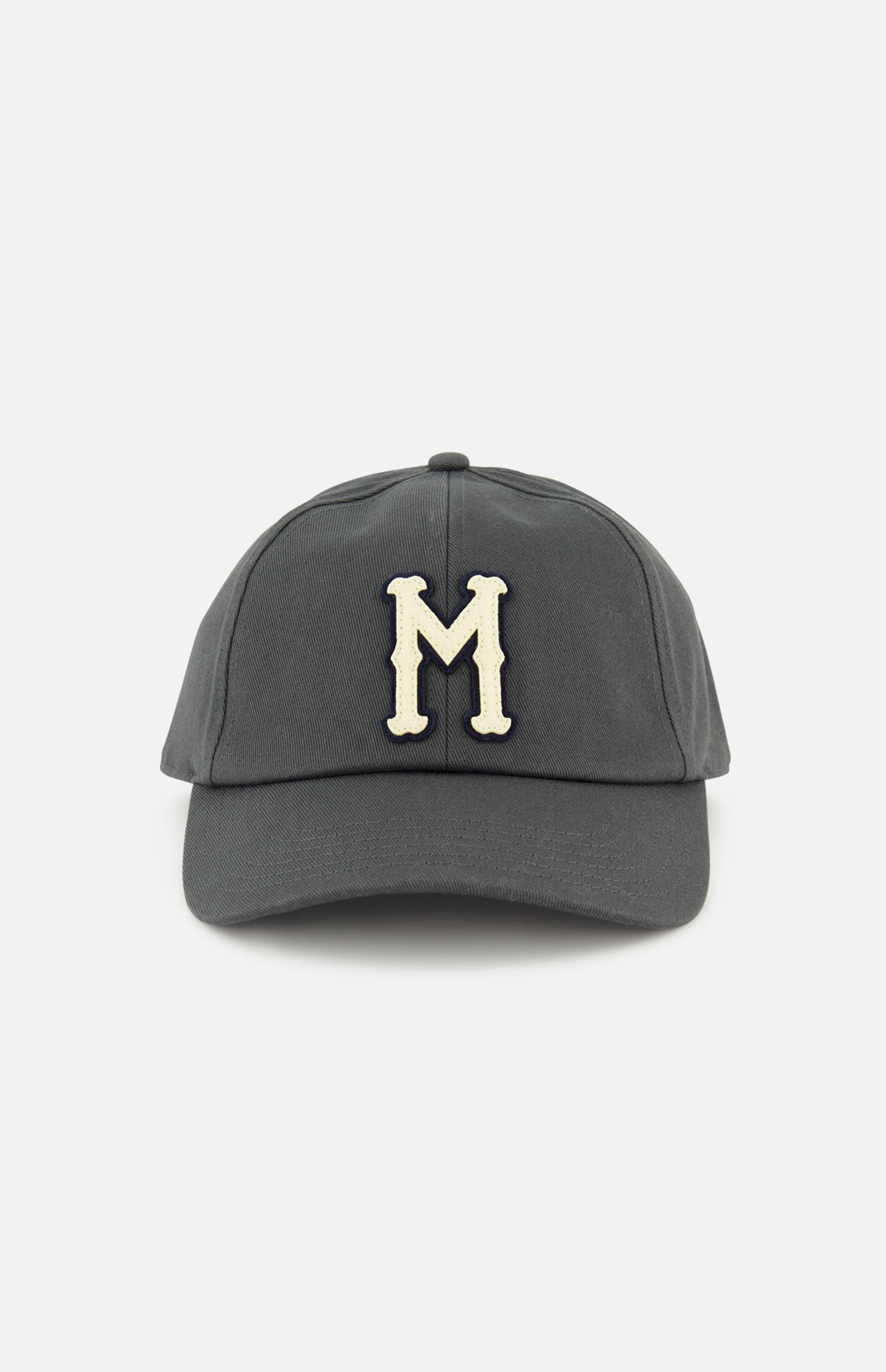 The MONCLER Monogram Baseball Cap features a grey design with a cream-colored embroidered letter M on the front, inspired by designer outerwear style, and is shown against a plain white background.