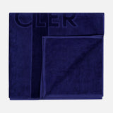 The MONCLER Logo Beach Towel, featuring a subtle embossed design and border in dark blue, is neatly folded and displayed on a light gray background.