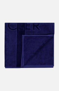 The MONCLER Logo Beach Towel, featuring a subtle embossed design and border in dark blue, is neatly folded and displayed on a light gray background.