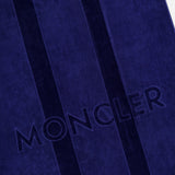 A close-up of the MONCLER Logo Beach Towel in deep blue, featuring two vertical stripes and the MONCLER name embossed on soft cotton—an ideal luxury accessory for seaside outings.