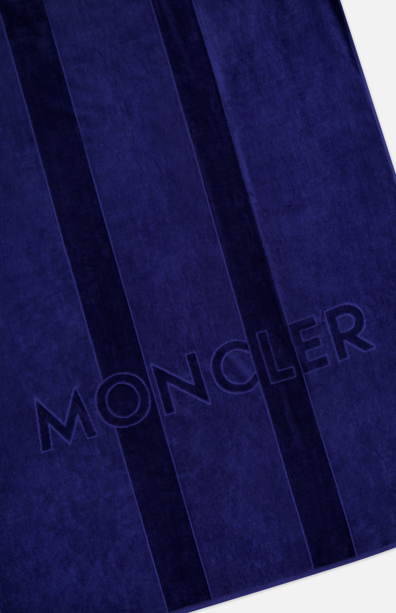 A close-up of the MONCLER Logo Beach Towel in deep blue, featuring two vertical stripes and the MONCLER name embossed on soft cotton—an ideal luxury accessory for seaside outings.