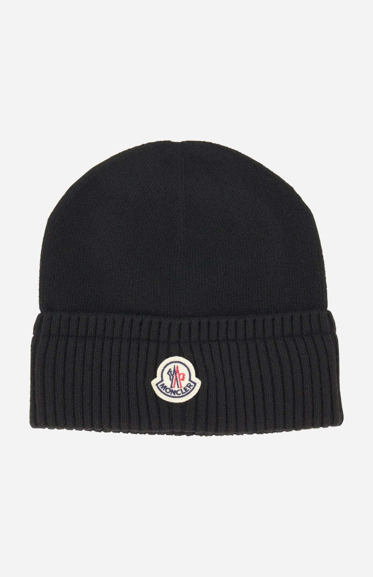The MONCLER Ribbed Logo Beanie is a black knit wool hat with a ribbed texture and folded brim, featuring the brand’s signature logo patch on the front center.