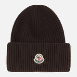 A dark brown MONCLER Contrast Logo Beanie crafted from virgin wool in a ribbed design, featuring a folded brim and a small contrast Moncler logo patch at the front center.