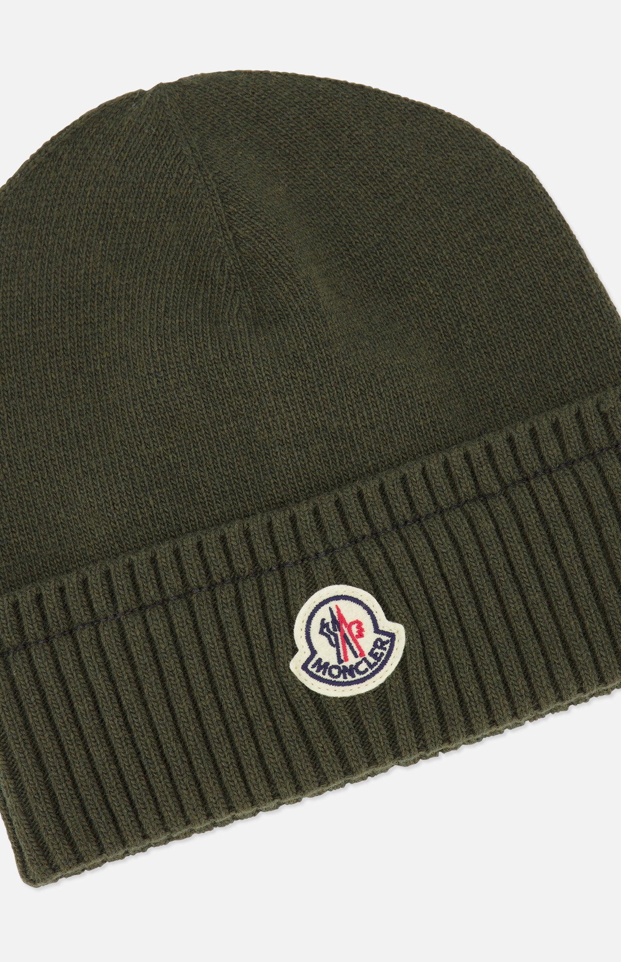 The MONCLER Ribbed Logo Beanie in dark green is crafted from virgin wool, featuring a ribbed design with a folded cuff and a round logo patch on the front.