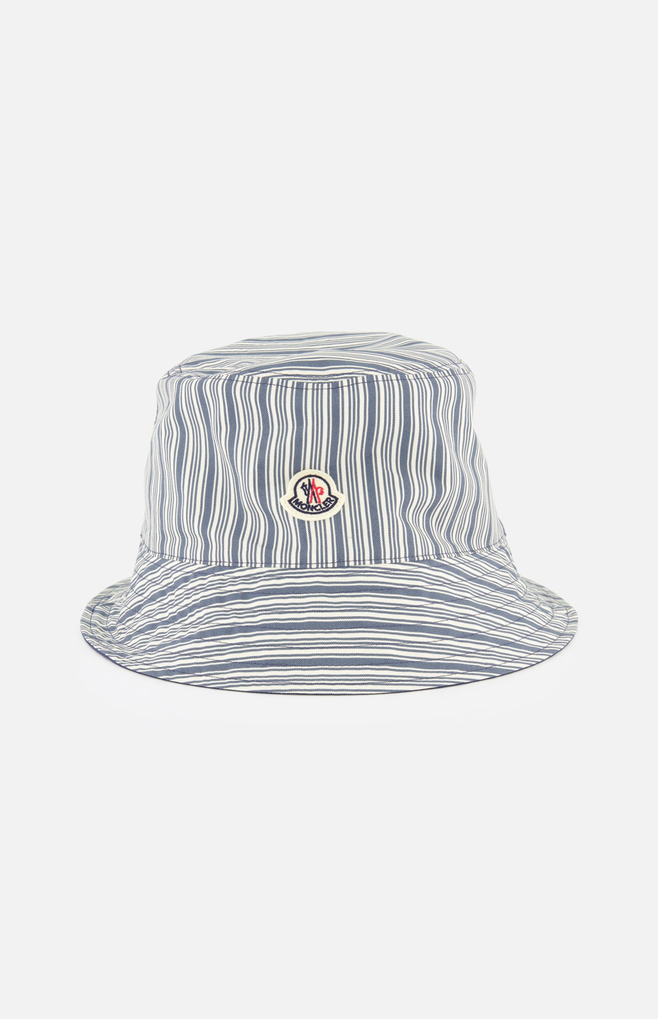 A MONCLER Reversible Bucket Hat, featuring blue and white vertical stripes and a round embroidered logo patch on the front, crafted from cotton, is shown against a plain white background.