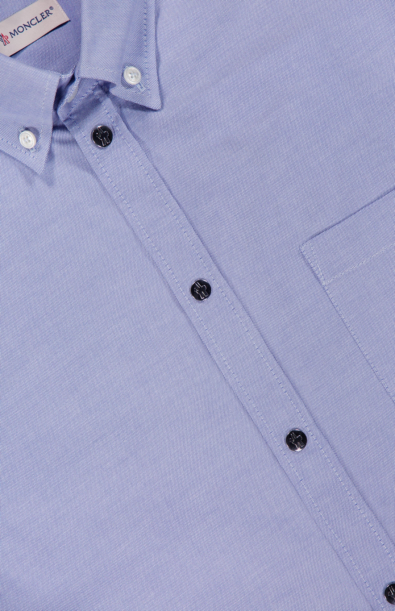 Close-up of the MONCLER Cotton Button Up Shirt in light blue with a front pocket, white stitching, black buttons, visible collar, and a partial MONCLER label at the top left for authenticity.
