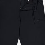 A pair of MONCLER Zip Pocket Stretch Pants in black is shown from the waist down, with the front partially unzipped to highlight the zipper, button closure, drawstring, and a visible inner tag. This stretch design also includes a small zip pocket on the right side.