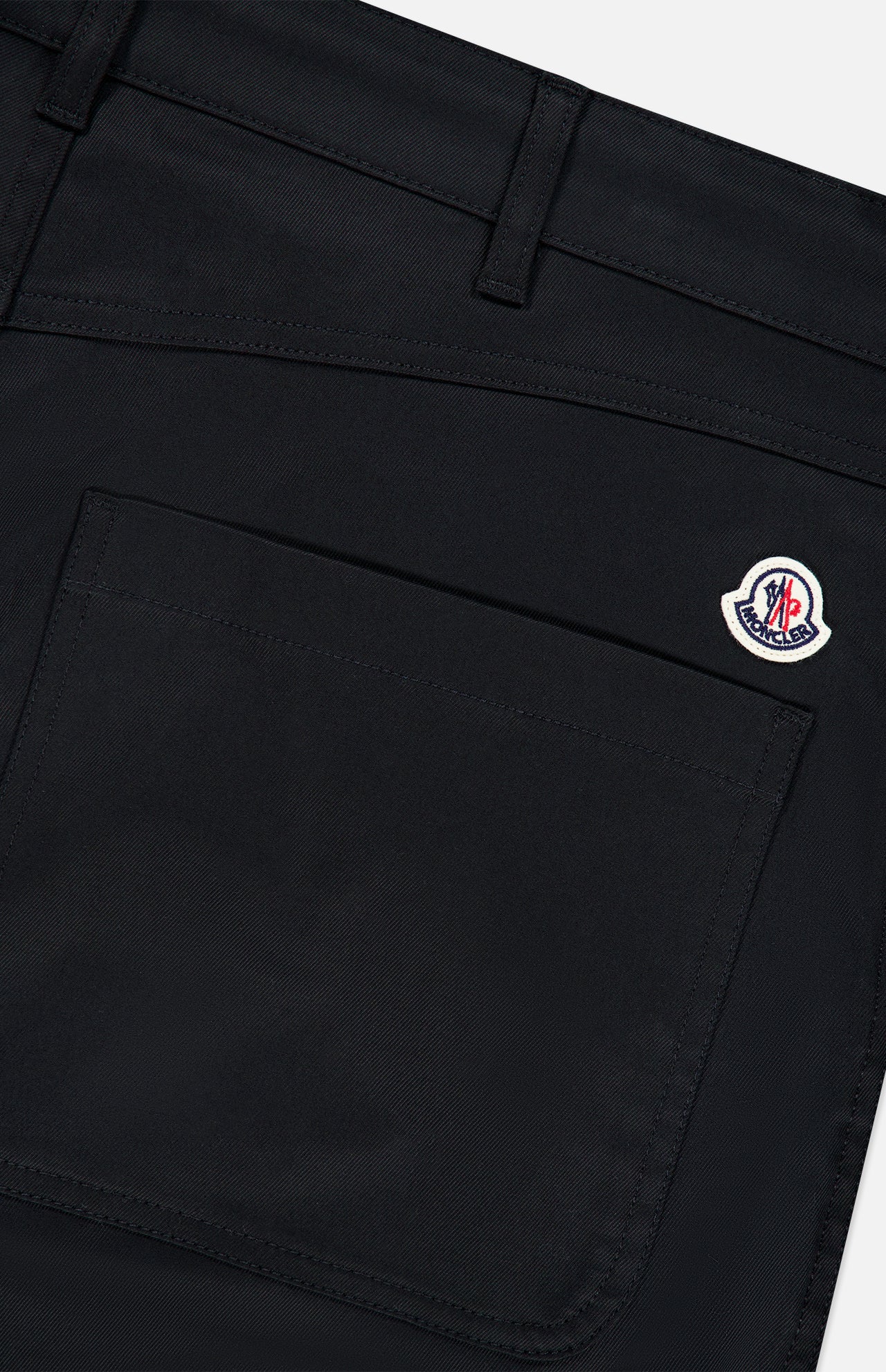 Close-up of the MONCLER Zip Pocket Stretch Pant in black, showcasing a sleek zip pocket topped with a subtle Moncler logo patch. Visible stitching and belt loops emphasize the structure and refined details of this stretch outerwear piece.