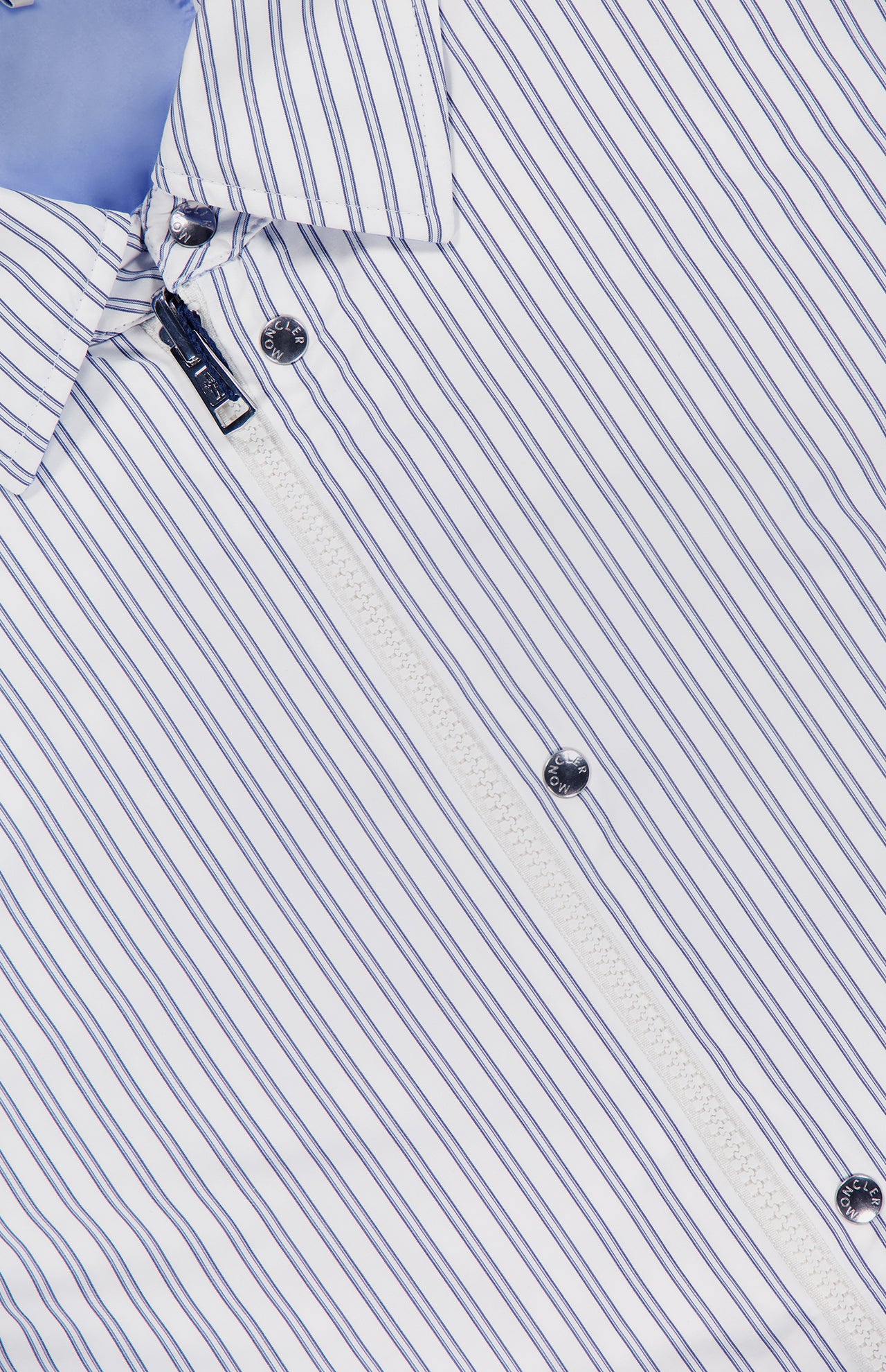 A close-up of the MONCLER Reversible Crescent Shirt Jacket in white with thin blue stripes, black buttons, and a diagonally unzipped white zipper—an elegant upgrade for men's outerwear.