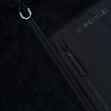 Close-up of the Fleeced Chest Pocket Vest by MONCLER, a black cold-weather essential featuring a zipper, a carabiner on the collar, and a zippered chest pocket adorned with the MONCLER logo in white letters.