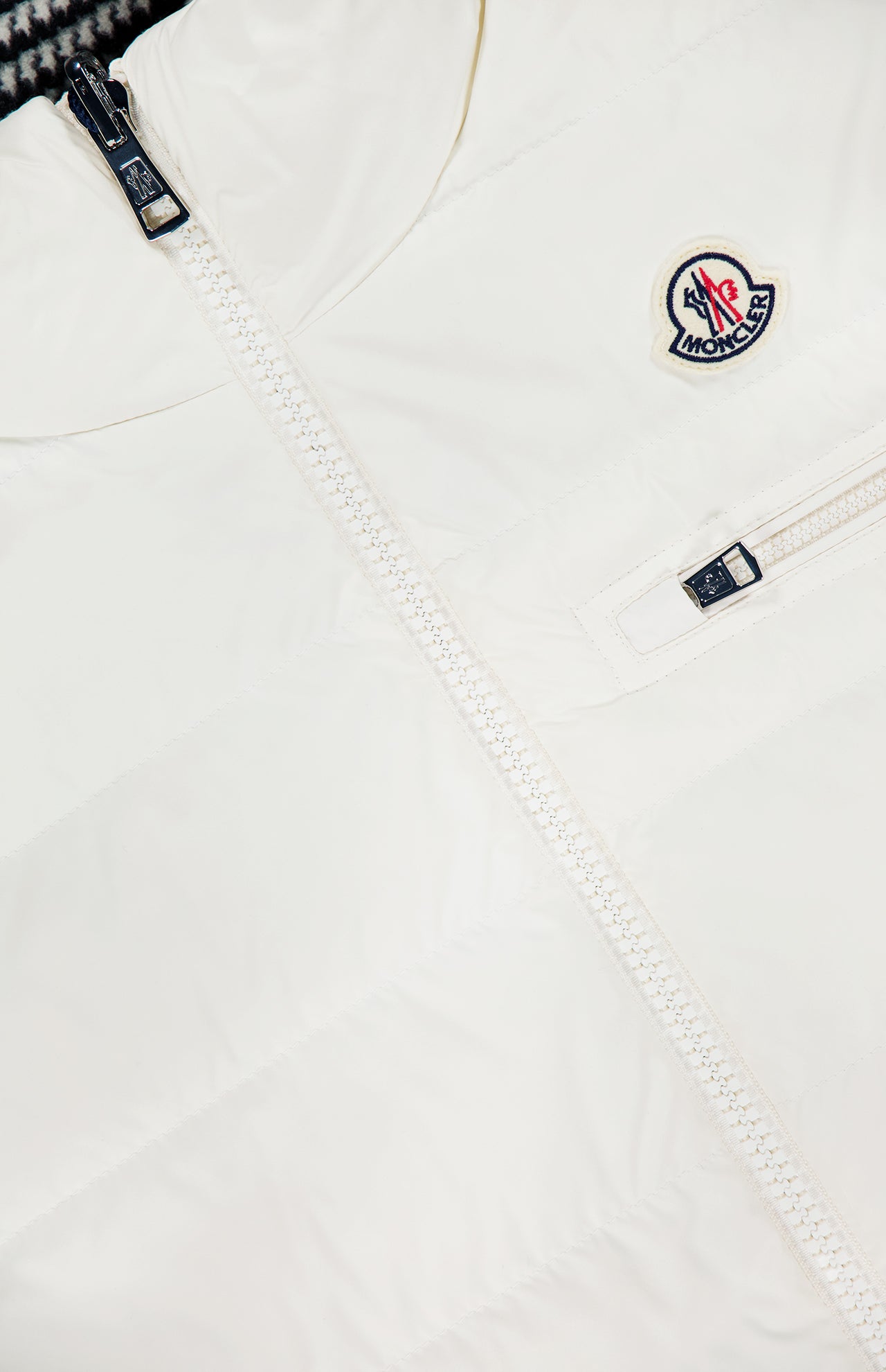 Close-up of the MONCLER Gienah Houndstooth Reversible Vest in white, featuring a visible zipper, small chest zip pocket, Moncler logo patch on the upper left, and smooth quilted fabric.