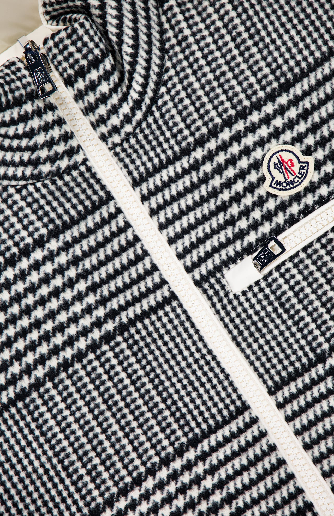 Close-up of the MONCLER Gienah Houndstooth Reversible Vest, featuring a houndstooth wool-blend, white zipper, Moncler logo patch on the chest, and a small zippered pocket.