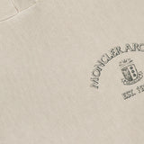 A close-up of the MONCLER Hoodie Logo Sweatshirt in beige highlights an embroidered crest and “MONCLER ARCHIVE EST. 1952” on the chest, with a soft, textured fabric.