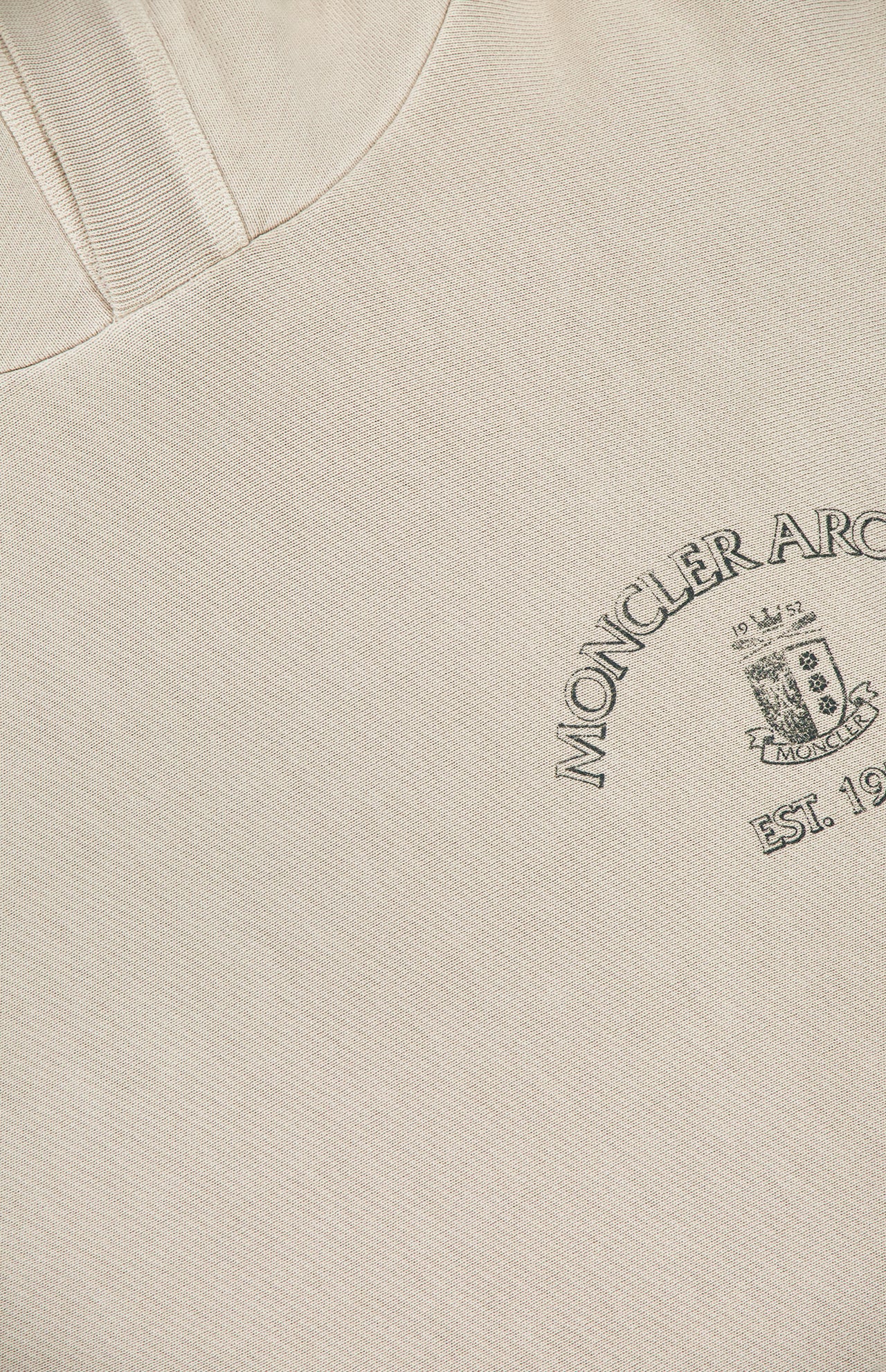 A close-up of the MONCLER Hoodie Logo Sweatshirt in beige highlights an embroidered crest and “MONCLER ARCHIVE EST. 1952” on the chest, with a soft, textured fabric.